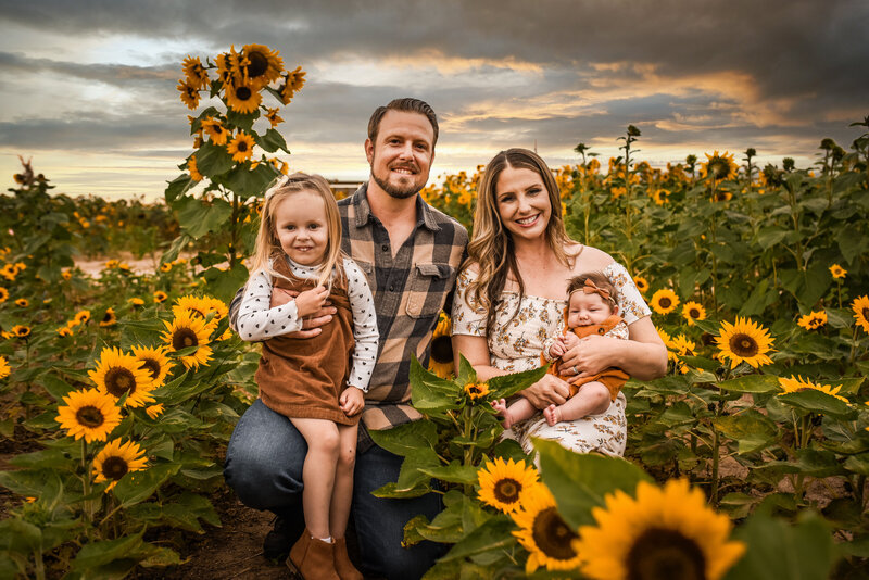 mother and father with two small children taking photo in sunflower field