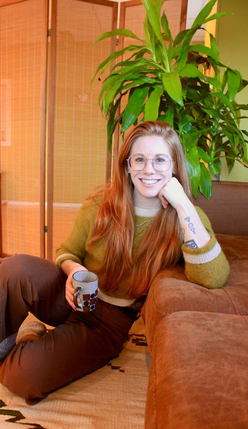 Licensed professional counselor, Emily, sits on the floor and leans against the couch in her office in Eugene.