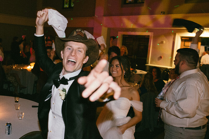 Smiling groom waves napkin overhead in celebration at his wedding reception.