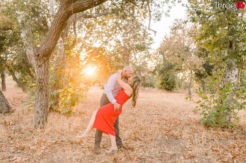 Groom to be dips his fiance while holding one of her legs up and kisses her under the welcome sign at the Irvine Regional Park