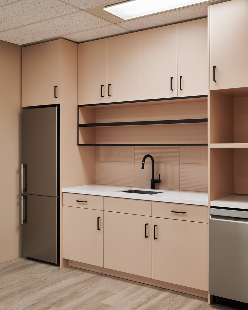 A cafe area kitchenette featuring cabinetry with a dusty pink finish and black accents, open shelves, and sleek silver appliances