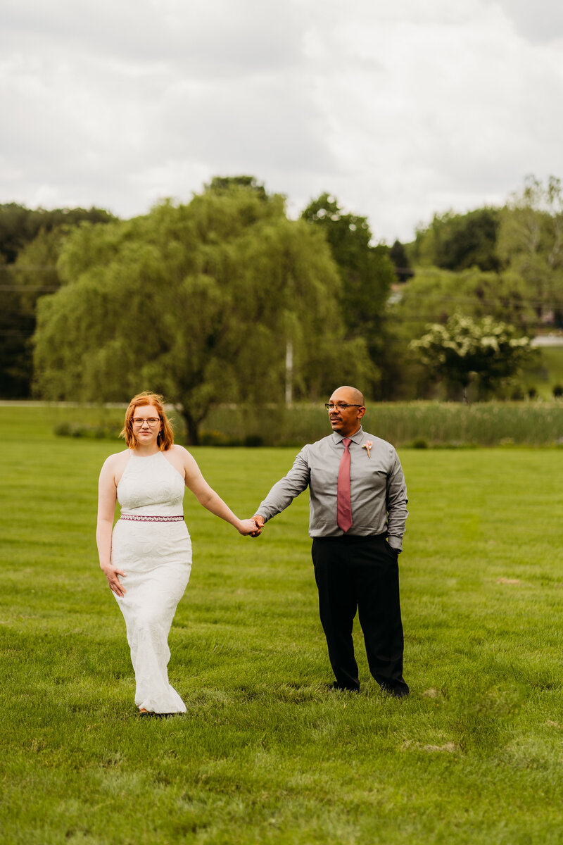 Bride and groom holding hands while walking through a green field during Virginia
elopement