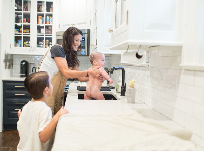 baby taking a bath in the kitchen sink while mom and brother help