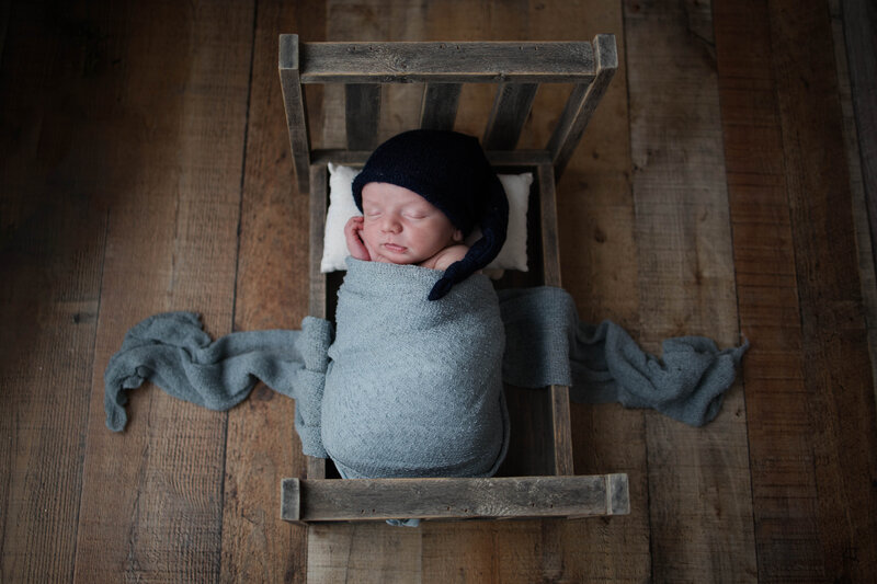 Newborn baby boy sleeping in newborn bed with a hat and blue blanket