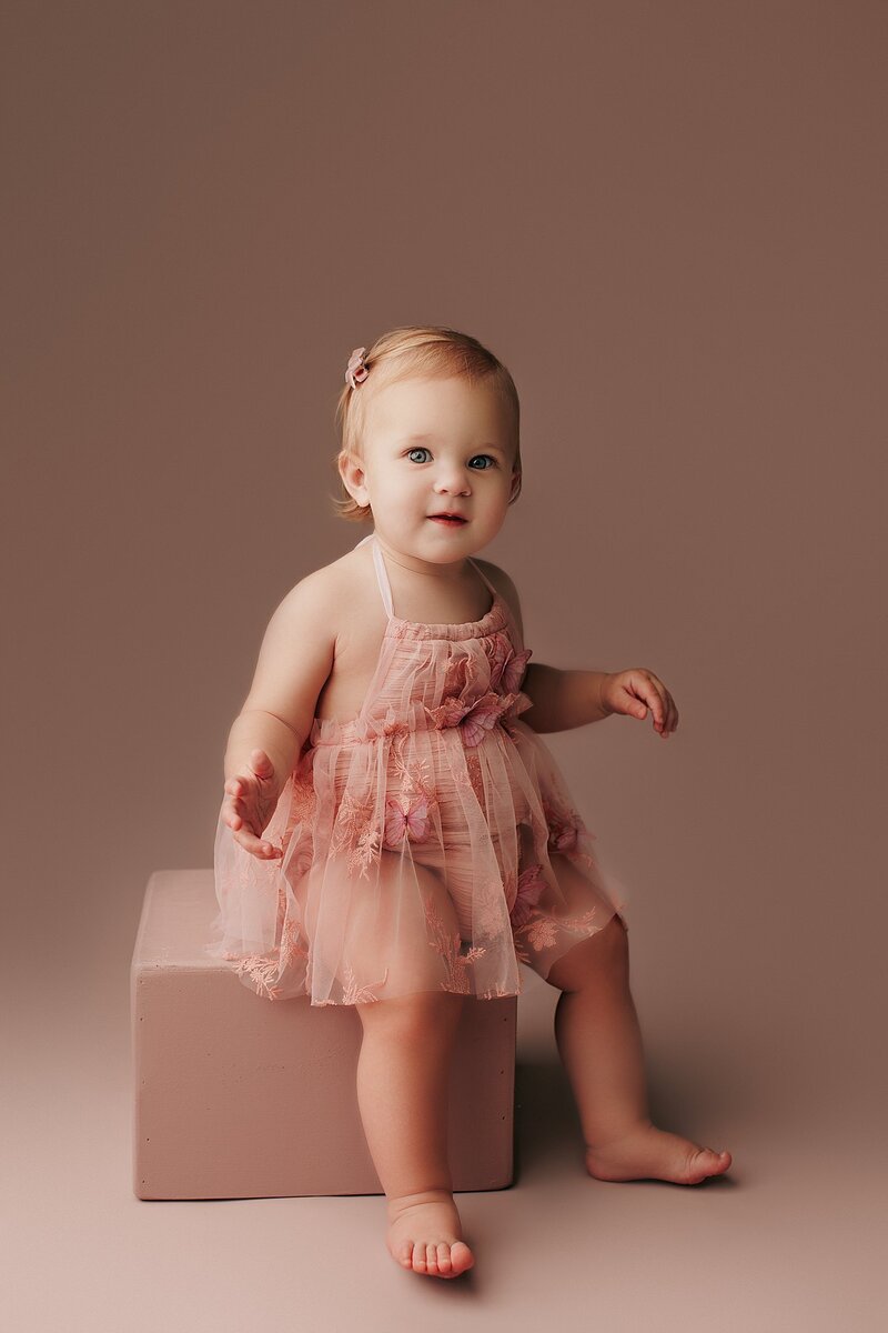 Baby girl smiling on soft pink studio backdrop during styled milestone session