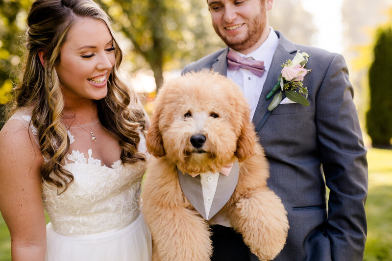 Bride and Groom holding their puppy who is wearing a tux too. Wedding at Barn at Murphey Farm