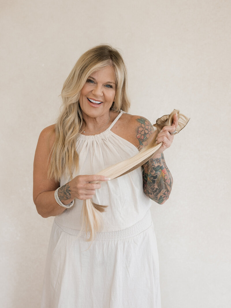 hair stylist dressed in white holding hair extensions