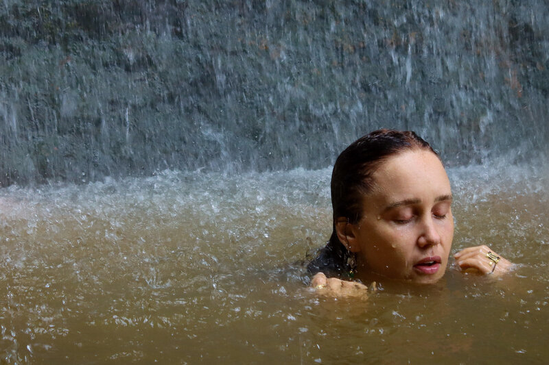 A portrait of a woman with her eyes closed basking under a waterfall in Bali, an example of Courtney's portraiture, retreat and event photography