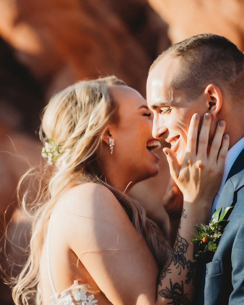 A Denver Bride kisses her new groom on the cheek in front of a small prop plane with a red sun flare. A plane themed private airfield northern colorado intimate wedding.