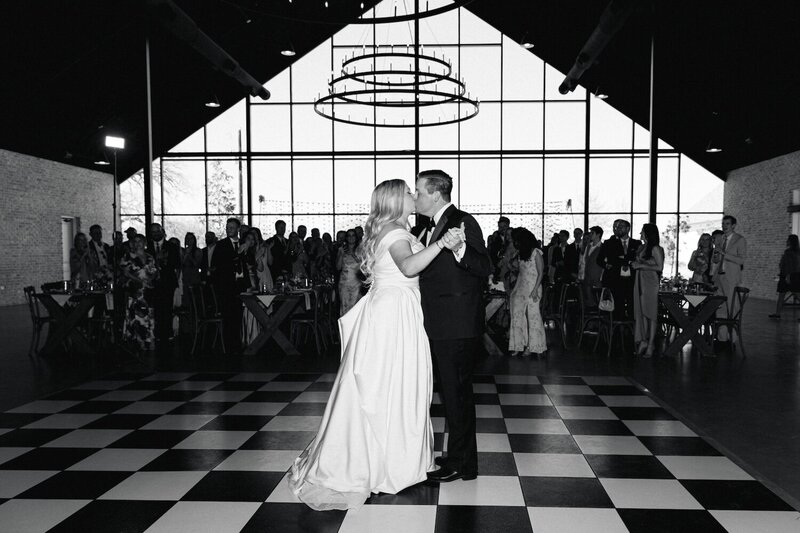 Bride and groom kissing during their first dance at Camp Hosea on a black and white checkered dance floor.