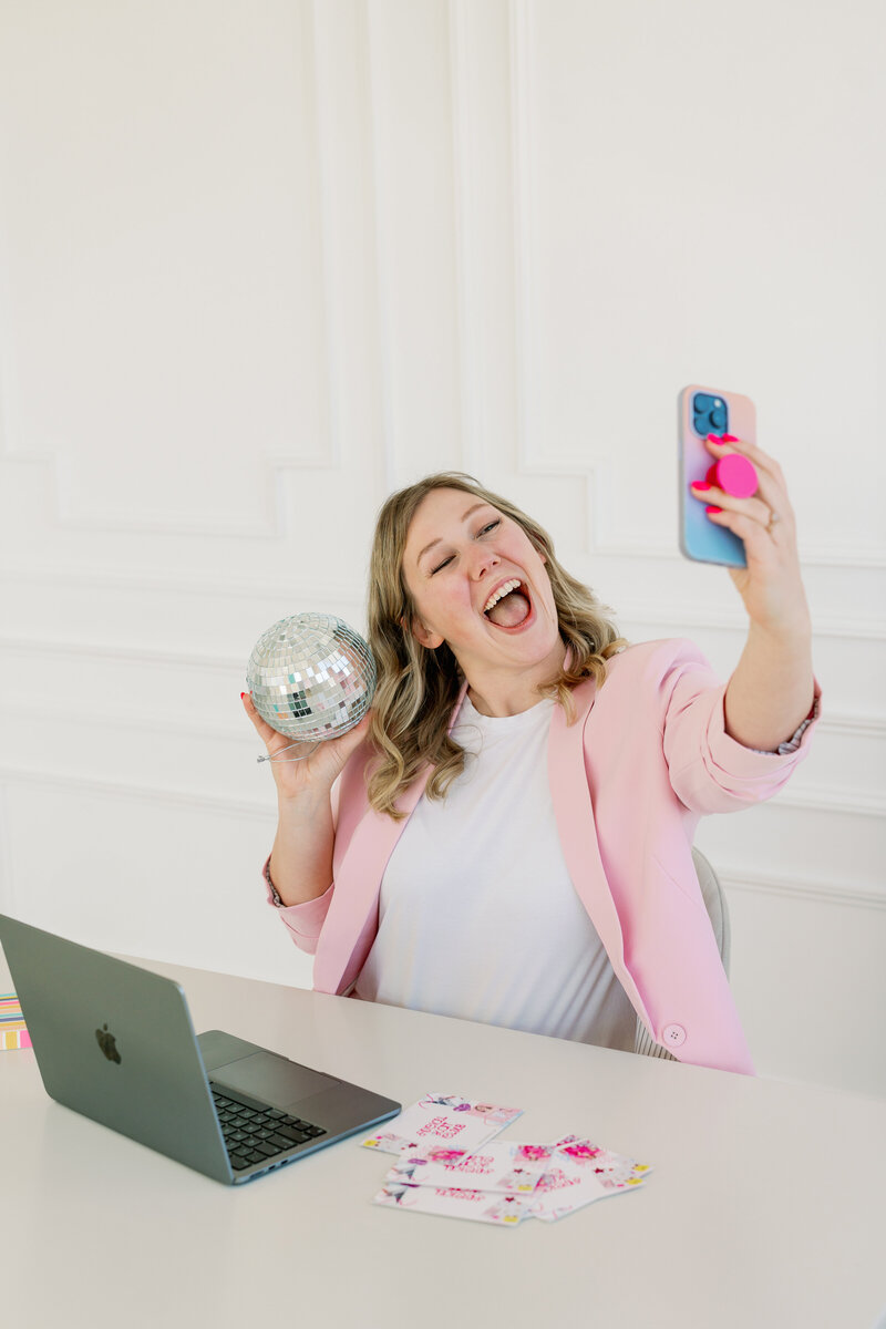 Kat Murphy in a pink jumpsuit typing on her iphone