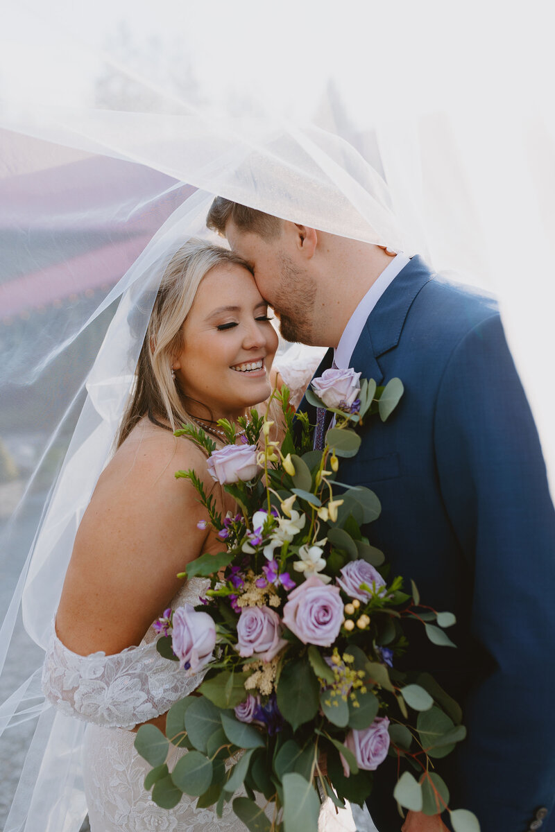 bride and groom hugging as she holds her purple flower bouquet
