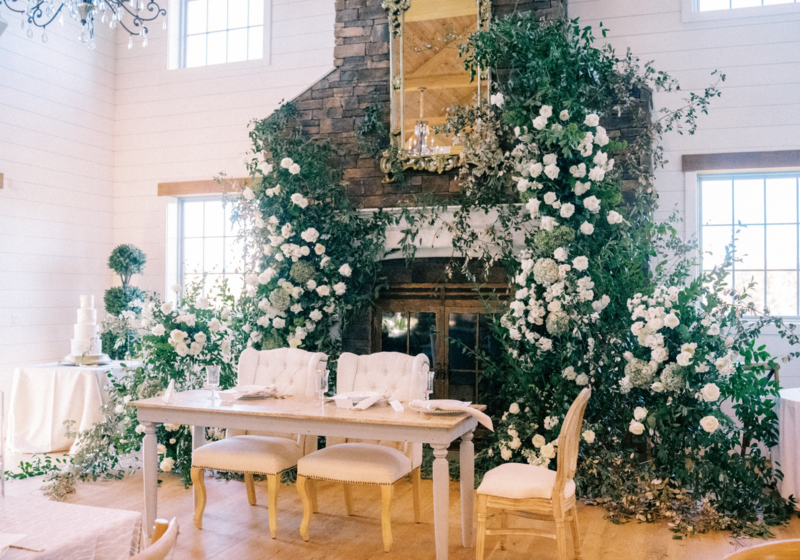 florals covering a mantle at a wedding reception with two chairs and a sweetheart table