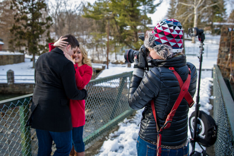 Jen Stitt standing with an engaged couple in the snow during a wintery engagement session in Lehigh Valley, capturing cozy and romantic moments in a picturesque frosty setting.