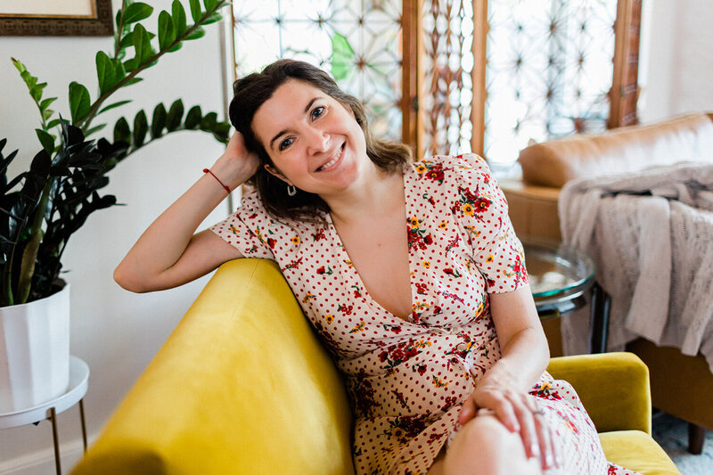 Photo of Andrea Shah sitting on a yellow couch, smiling and resting her head on her arm