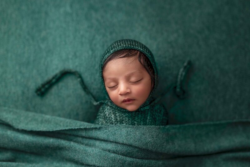 Sleeping Tacoma Baby laying on fabric with bonnet and green folded blanket covering his body.