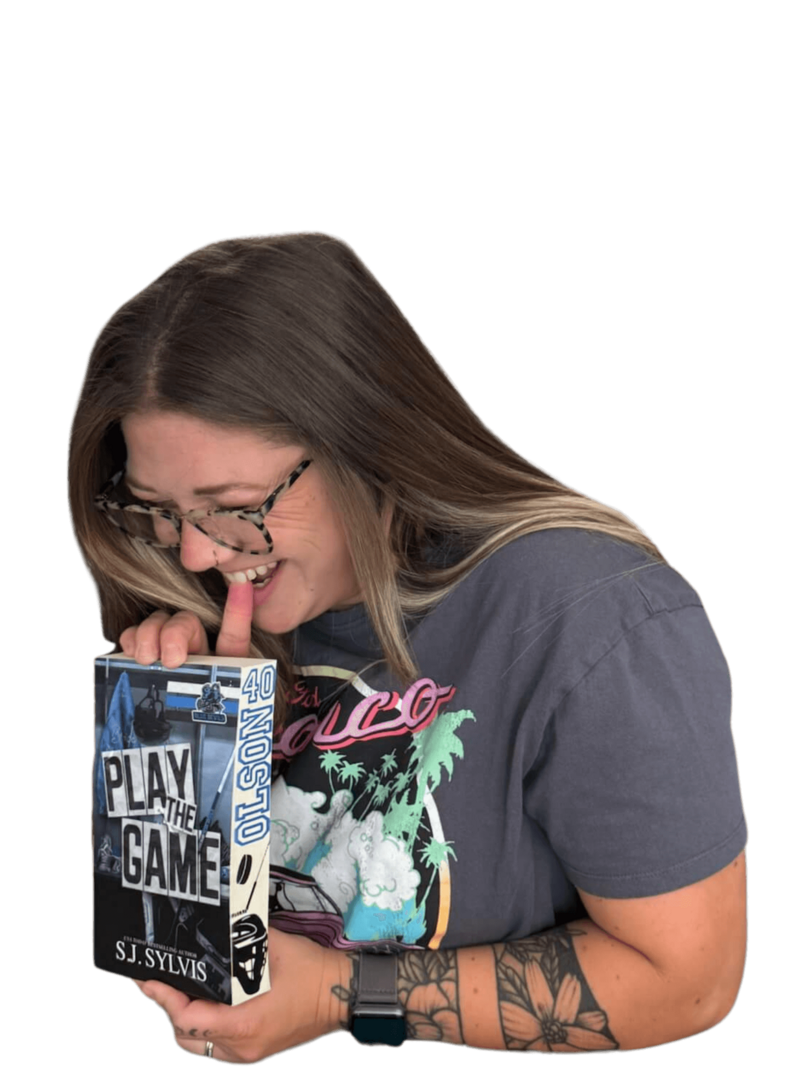 Courtney posing with a handmade sprayed-edge book from Sprayed Your Pages, holding it to her chest in a playful, expressive moment that captures her love for bold book designs.