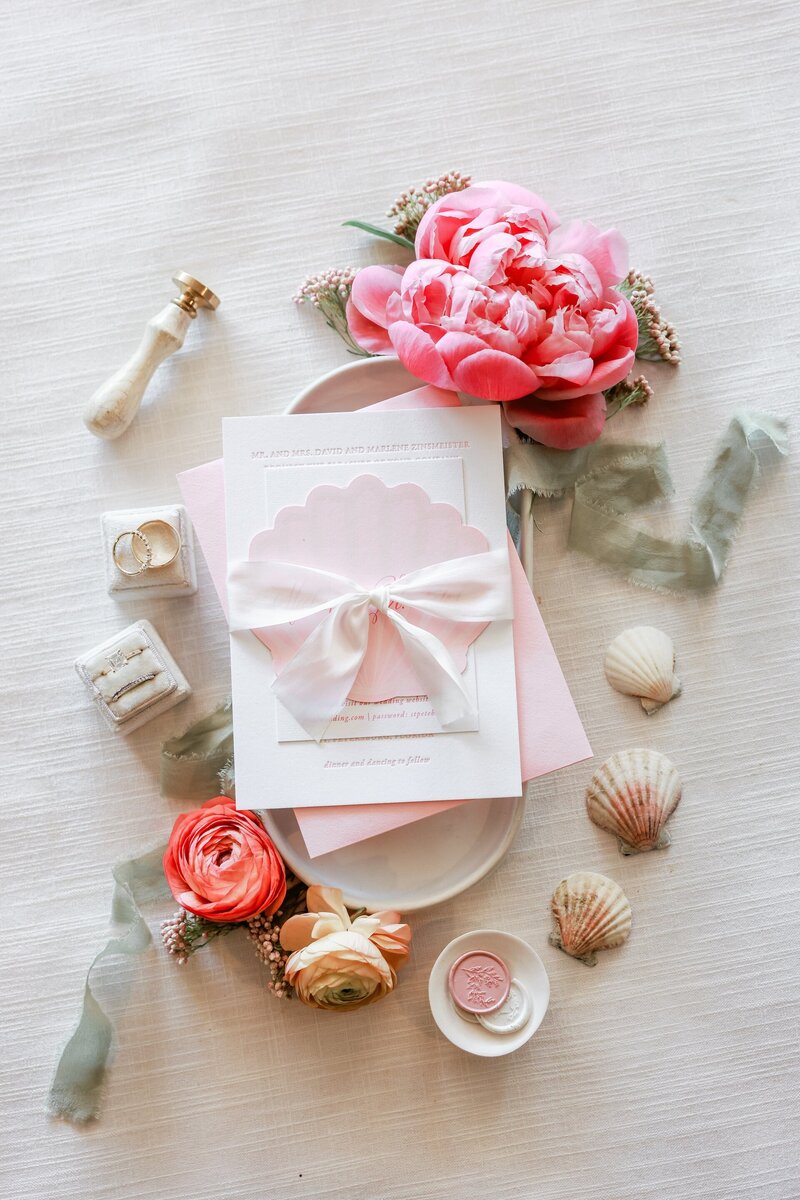a wedding invitation flat lay with pink flowers and seashells