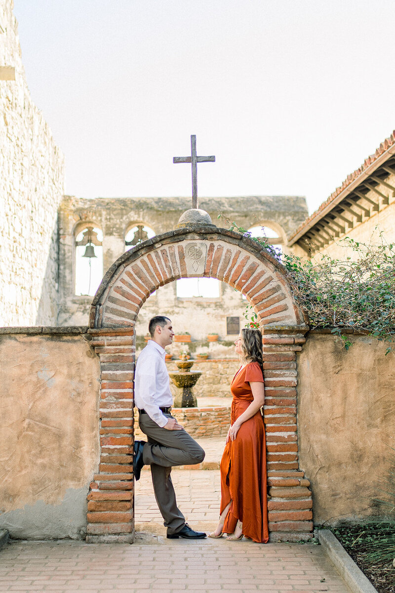 A couple stands under a stone archway at the historic Carmel Mission in California, captured by Tiffany Longeway Photography