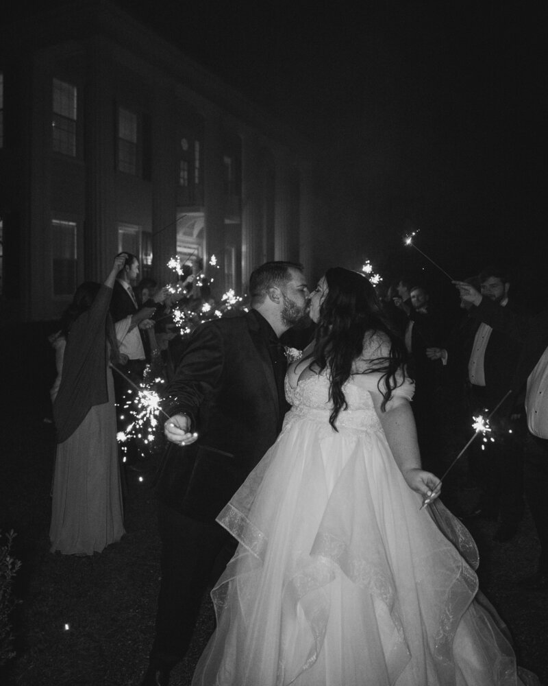 Bride and groom leaving their wedding at Englund Estate stop for a kiss while holding sparklers with their guests.