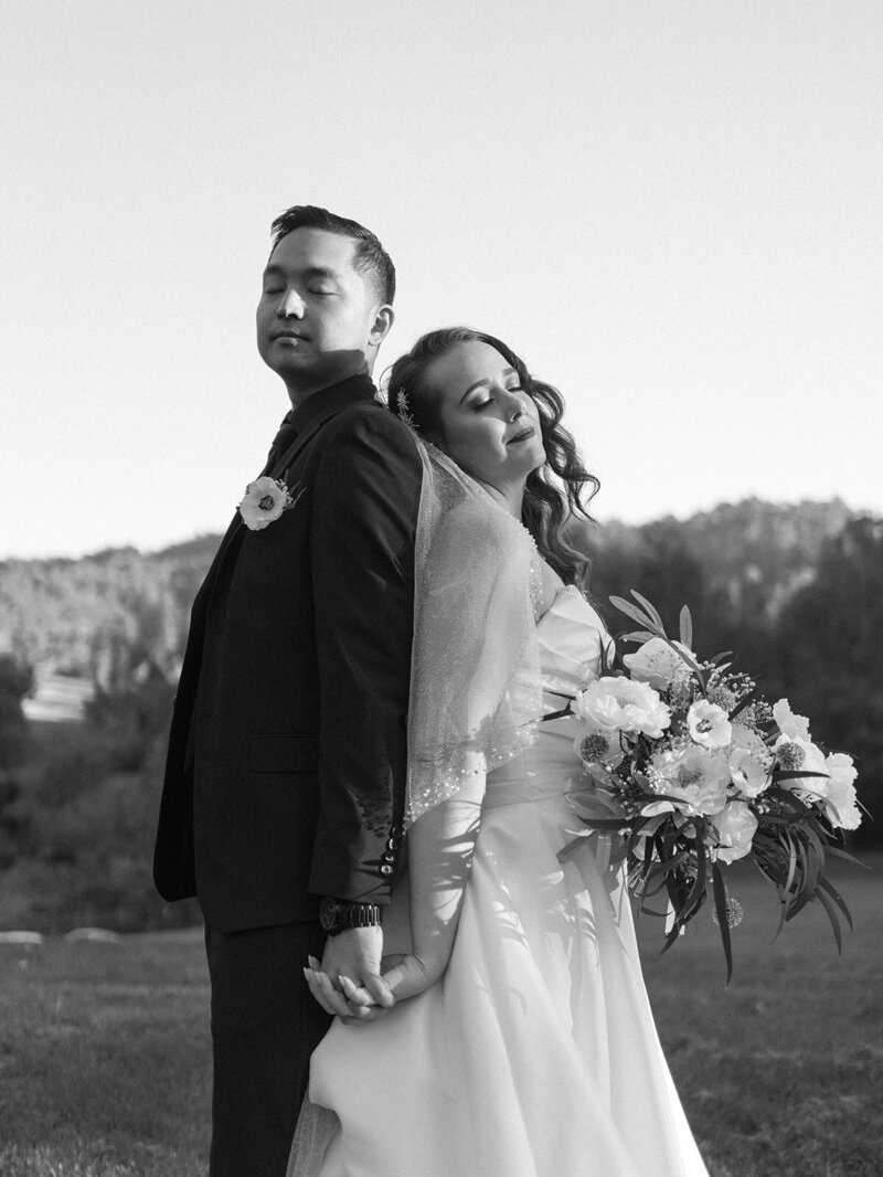 A black and white photo of a married couple standing back to back