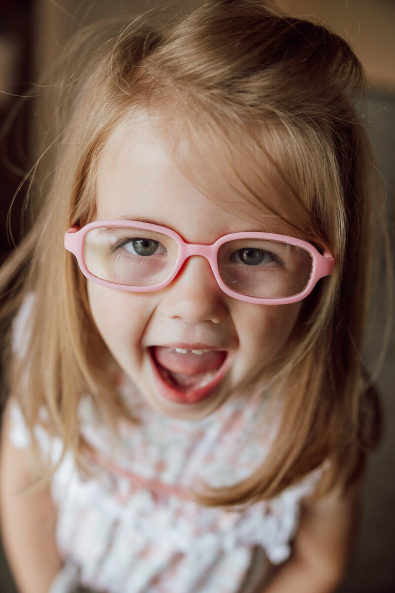Headshot of a young girl wearing pink glasses smiling at the camera. 