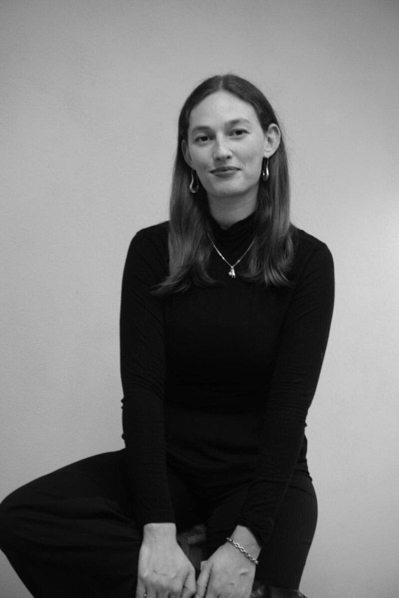 Cora Demary in a black turtleneck, seated and looking forward.