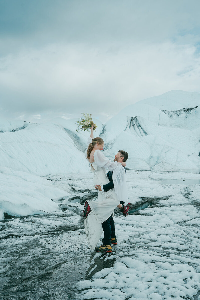 A newlywed couple with their arms around each other standing head to head 