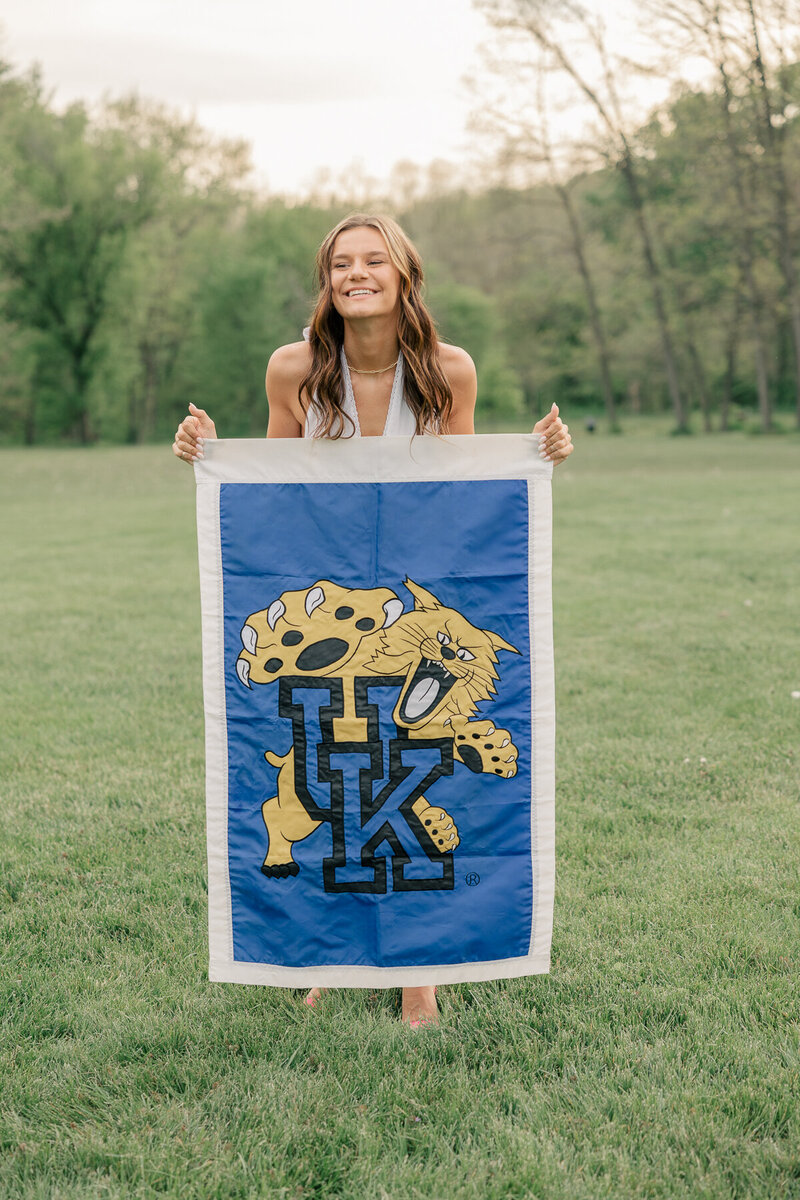 girl holding kentucky university flag and smiling in an open field, Indianapolis senior photographer