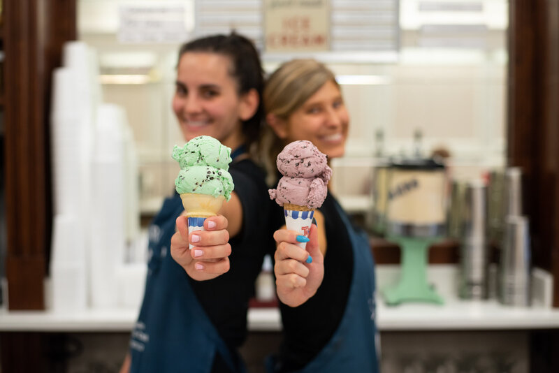 Two woman each holding an ice cream cone in an ice cream parlor.