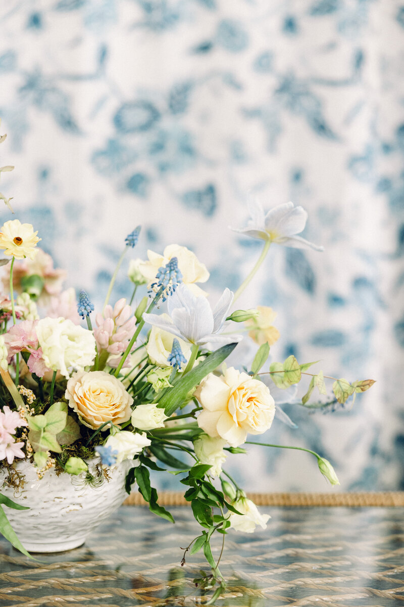White vase with pastel flowers, blue patterned background.