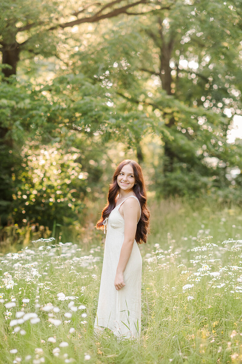 Senior girl in a white dress standing in wildflowers by York PA photographer