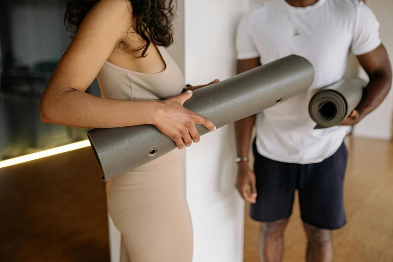 A man and woman stand together, each holding a yoga mat, ready for a class at Zenith Yoga and Pilates Studio.
