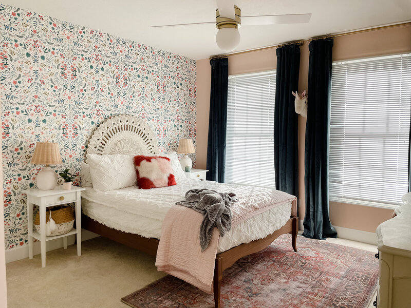 Dainty bedroom with an antique bed frame, colorful wallpaper with an intricate pattern and a pink throw blanket