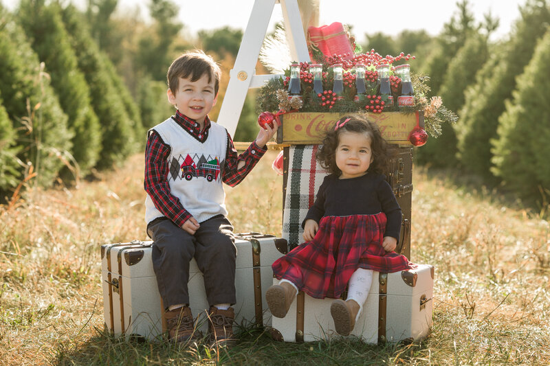 Two kids surrounded by festive Christmas props and trees during a holiday mini session in Greater Philadelphia