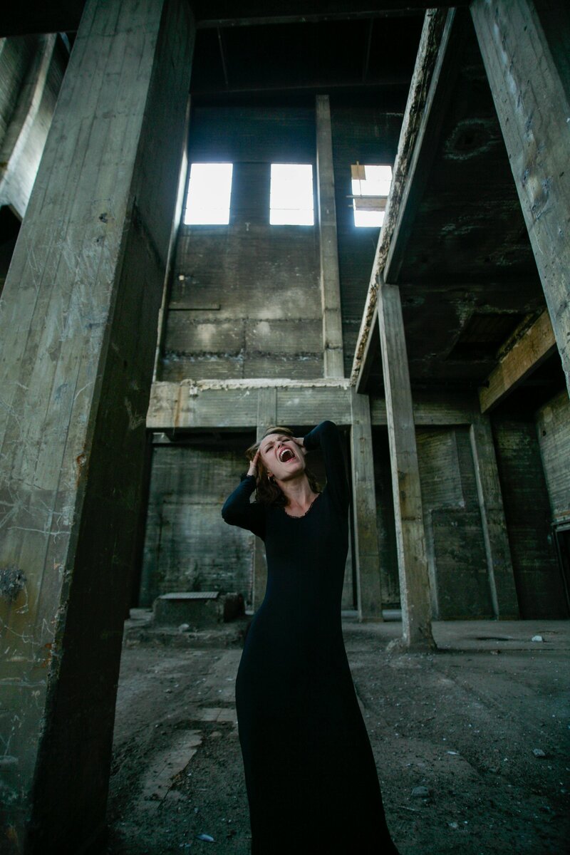 woman standing in a long black dress screaming and holding her head