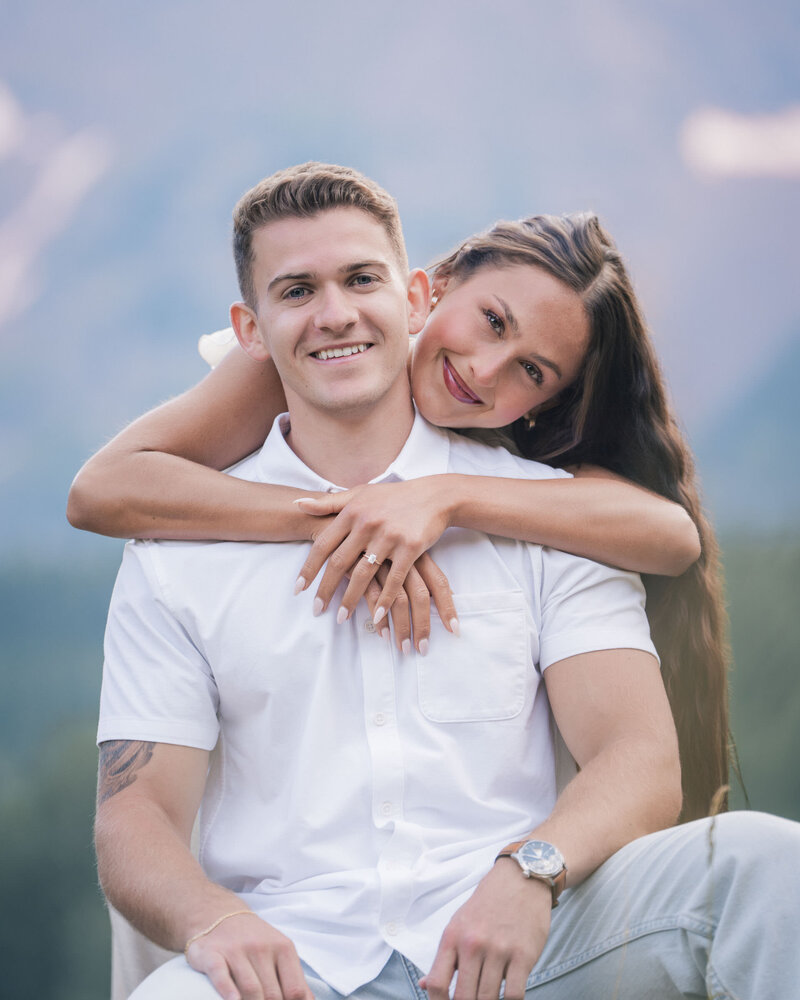 Smiling couple sharing a piggyback moment during a mountain engagement session