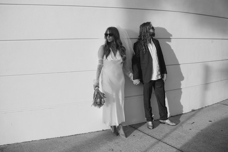 Black-and-white photo of a bride and groom holding hands outdoors, styled by Tyler and Makenzie Films, luxury wedding videographers