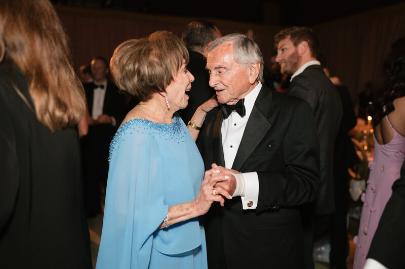 Black and white photo of the father of the bride looking out a window while the bride fixes her veil. Photo by Anna Brace an Omaha NE Wedding Photographers.