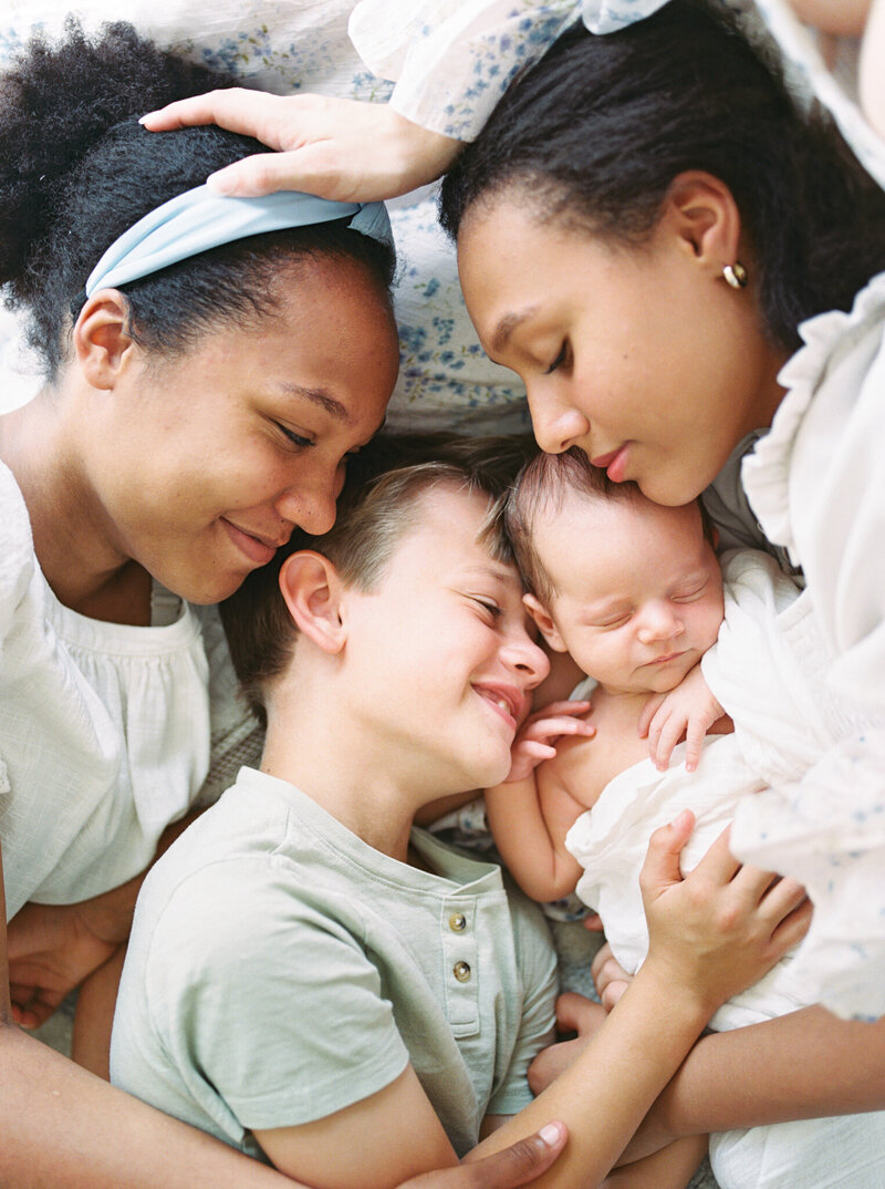 A newborn boy lying surrounded by caucasian older brother and two black sisters as they smile and snuggle him taken by photographer Little Rock Bailey Feeler