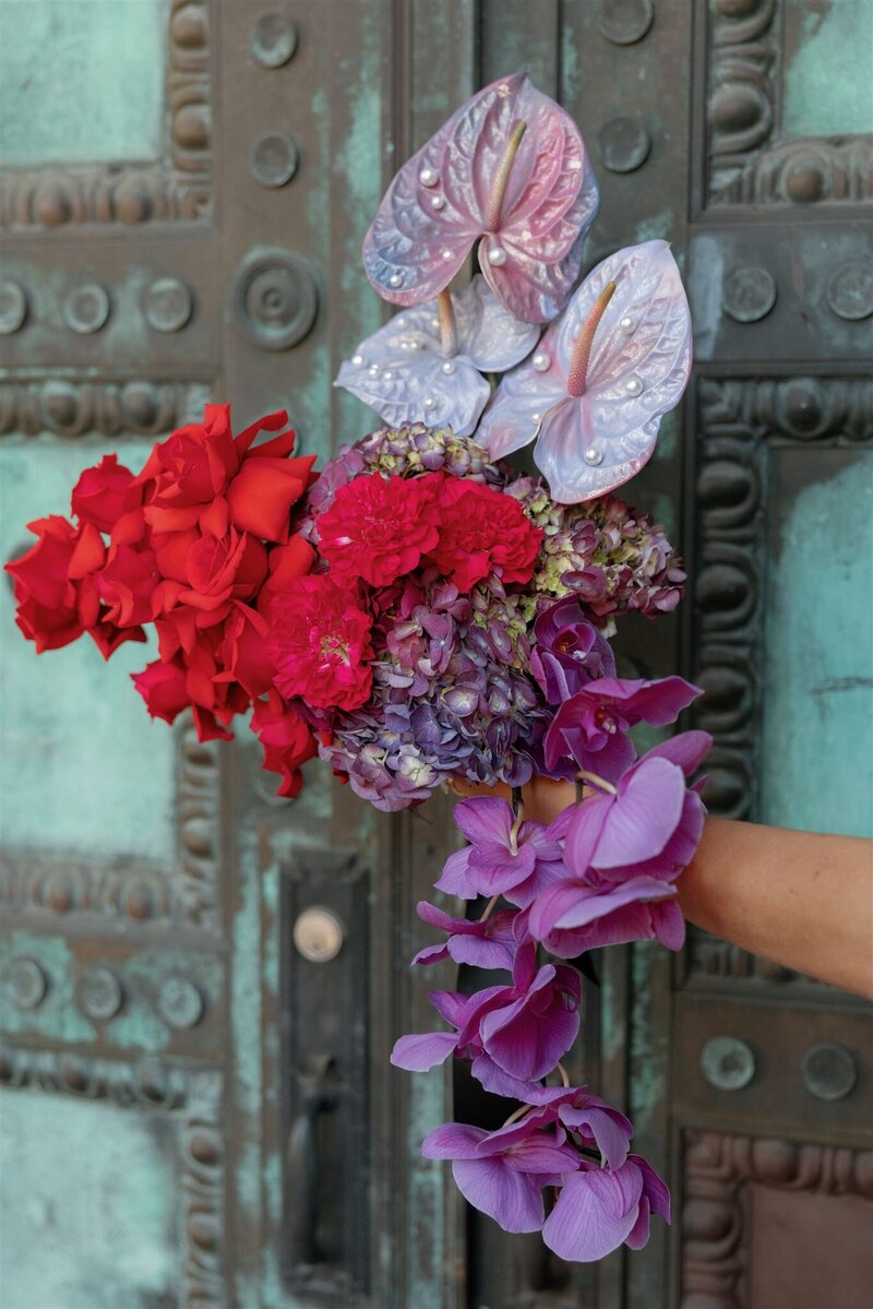 modern bright red, pink, lavender cascading bridal bouquet with iridescent spray painted anthuriums with pearls in front of a vintage oxidized bronze door