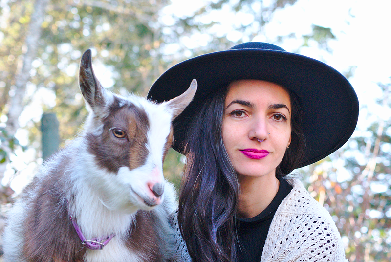 Pet Psychic wearing brimmed hat and her small spotted goat face to face. 