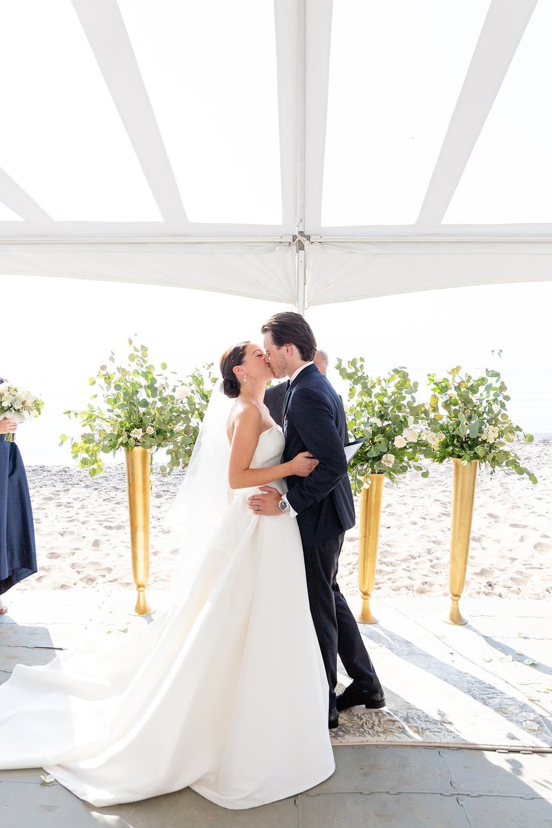 Bride and groom share their first kiss as husband and wife on their wedding day on the beach of Zurich Ontario