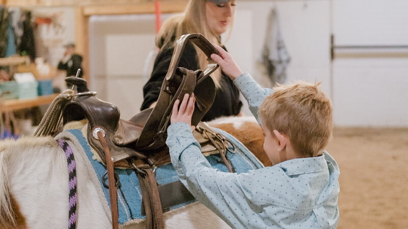 A child adjusting the saddle on a horse at Spirit’s Respite Ranch