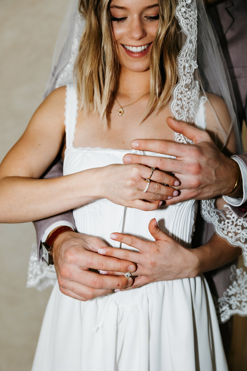 Flash photo of a bride in a veil and groom behind her touching each other's wedding rings