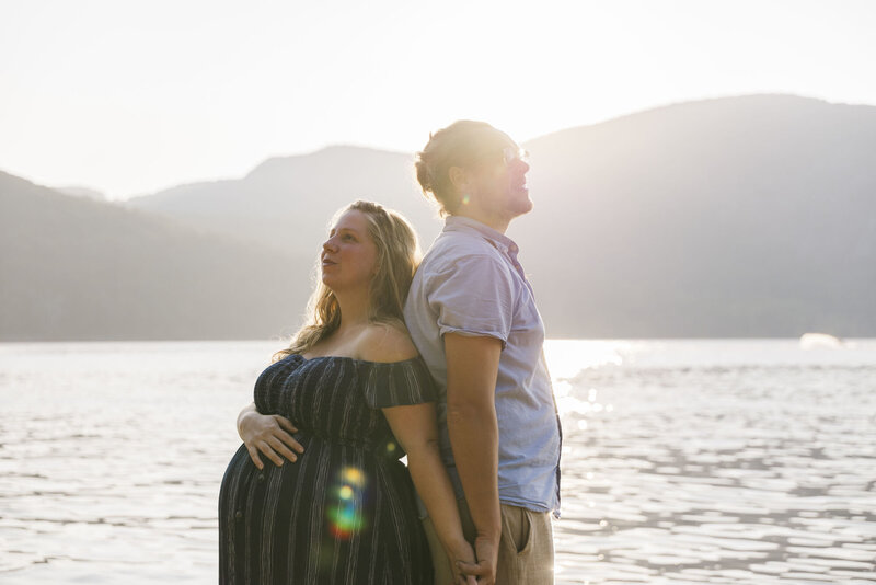 Expecting couple standing back to back by the Hudson River at sunset during a maternity session