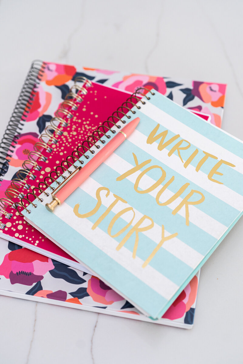 Three colorful notebooks on a table with the top notebook that says Write Your Story with a pen on top.