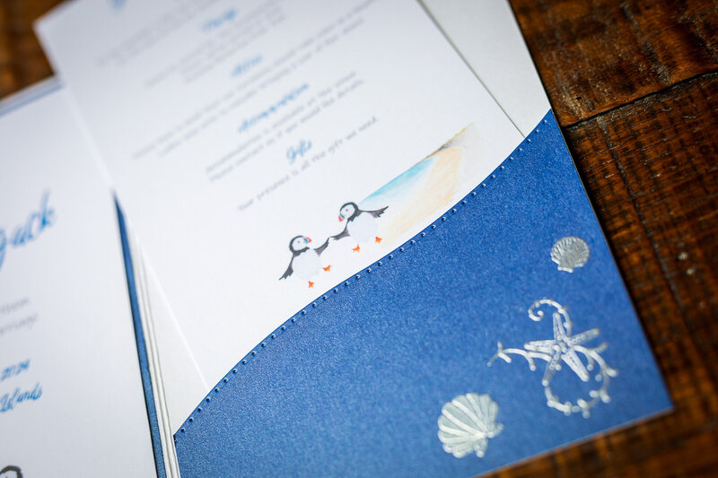 Wallet-style wedding invitation featuring watercolour puffins and embossed shells