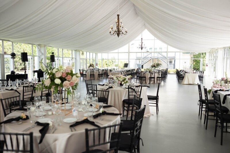Wide view of wedding reception at Ritz Charles glasshouse venue featuring chandeliers, round tables, and cream linens.