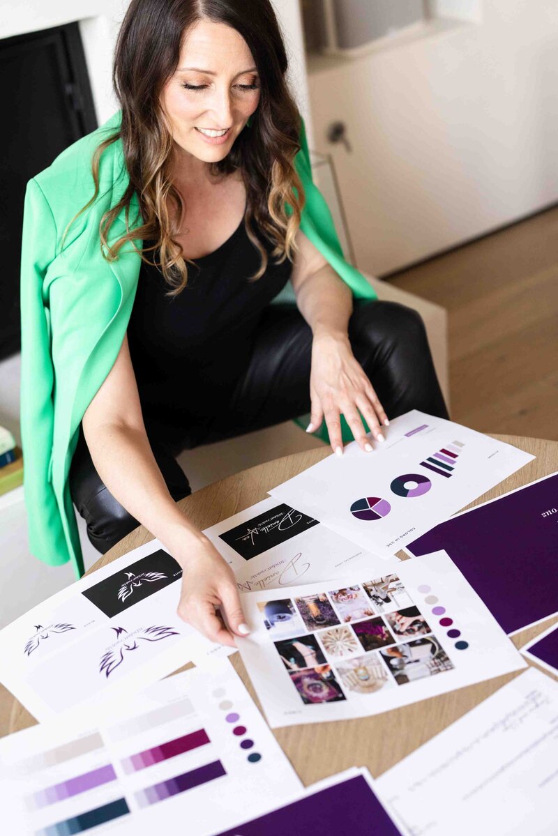 Luxury brand strategist in emerald green blazer reviewing client brand board with custom mood board, color palette, and visual identity elements during strategic design consultation